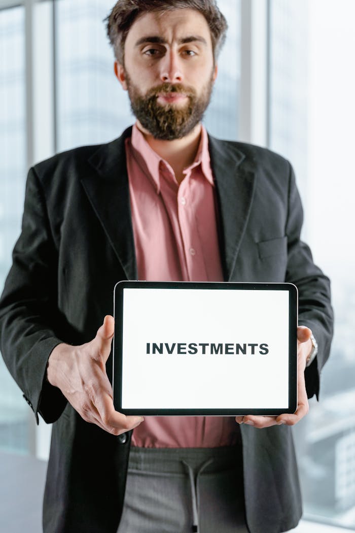 team-03 Businessman holding tablet displaying the word 'Investments' in an office setting.
